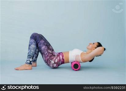 Woman performs myofascial relaxation of the hyperflexible muscles of the back with a massage roller on a blue background. The concept of prevention of back fatigue and self-massage