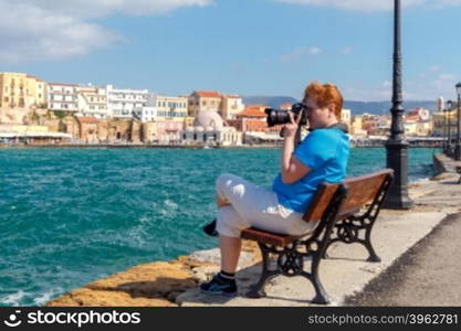 Woman photographer photographs the old harbor in Chania. Greece. Crete.. The woman with the camera on the waterfront of Chania.