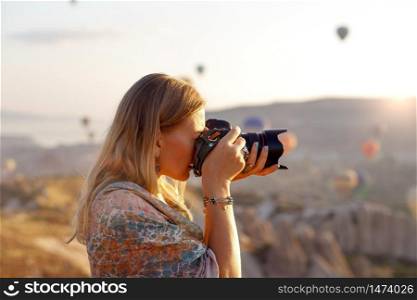 Woman photographer takes pictures of flying hot air balloon at dawn in Cappadocia, Turkey. Travel concept. Dressed in a scarf with a Turkish national pattern Ebru