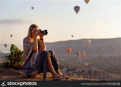 Woman photographer takes pictures of flying hot air balloon at dawn in Cappadocia, Turkey. Travel concept. Dressed in a scarf with a Turkish national pattern Ebru