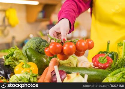 Woman picking tomatoes from healthy colorful vegetables on kitchen table. Dieting, vegetarian local fresh food, natural source of vitamins.. Many healthy colorful vegetables