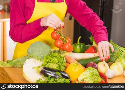 Woman picking tomatoes from healthy colorful vegetables on kitchen table. Dieting, vegetarian local fresh food, natural source of vitamins.. Many healthy colorful vegetables