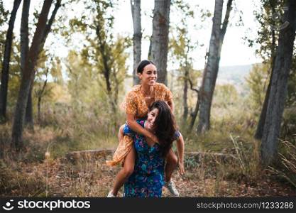 Woman piggybacking happy girlfriend while enjoying on the forest