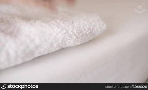 Woman placing a clean fresh white towel on a bed and then smoothing it with her hands