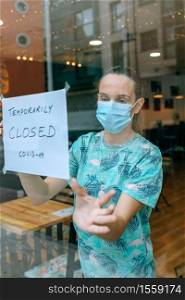 Woman placing a coronavirus closure sign in a coffee shop. Woman placing coronavirus closure sign