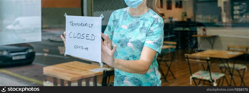 Woman placing a coronavirus closure sign in a coffee shop. Woman placing coronavirus closure sign