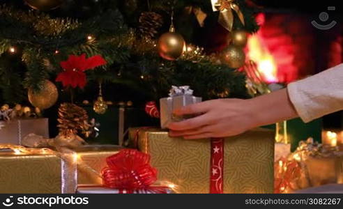 Woman placing gifts under Christmas tree near fireplace. Dolly shot