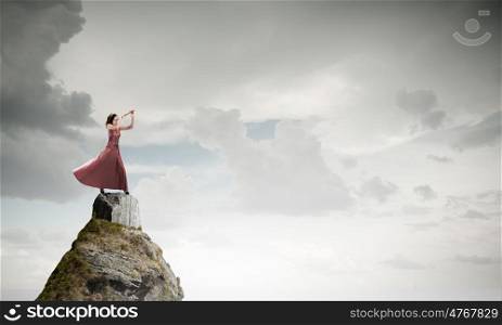 Woman play fife. Young woman in evening dress on rock playing fife