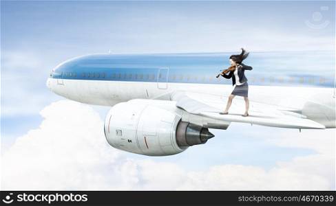 Woman play violin. Young businesswoman standing on edge of airplane wing and play violin