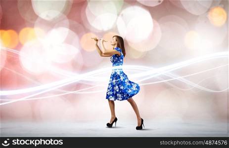 Woman playing fife. Young woman in blue dress playing fife against bokeh background