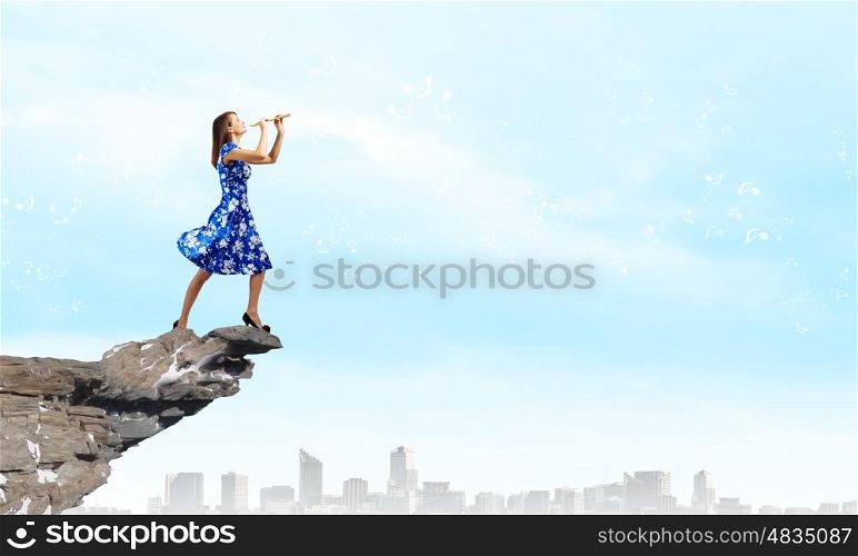 Woman playing fife. Young woman in blue dress playing fife standing on top of rock