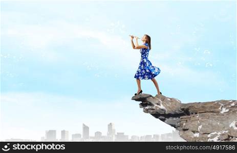 Woman playing fife. Young woman in blue dress playing fife standing on top of rock