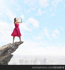 Woman playing fife. Young woman in red dress on edge of rock playing fife