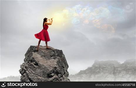 Woman playing flute. Young woman in red dress on rock playing fife