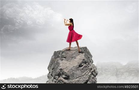 Woman playing flute. Young woman in red dress on rock playing fife