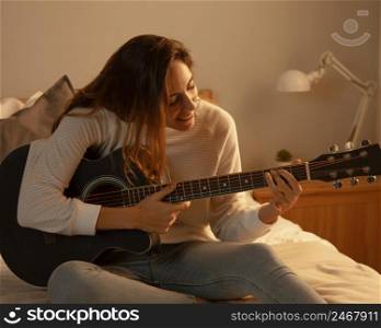 woman playing guitar home bed