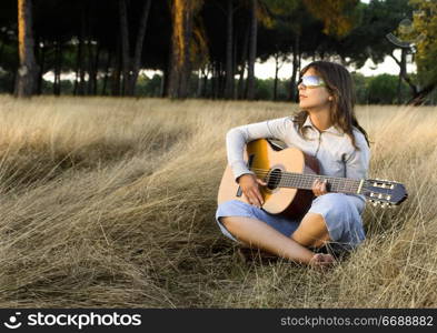 Woman playing her guitar on a meadow at the sunset