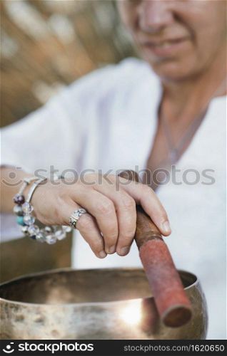 Woman playing on Tibetan singing bowl outdoors . Sound Therapy with Tibetan Singing Bowl
