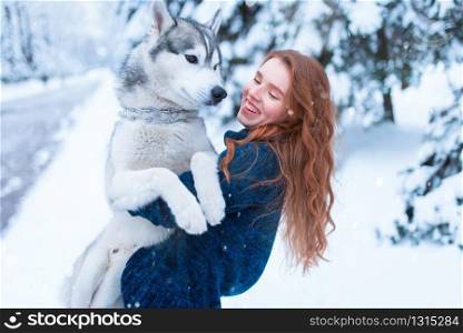 Woman playing with siberian husky, friendship forever, snowy forest on background. Cute girl walk in park with playful pet