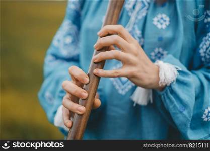Woman playing woodwind wooden flute - ukrainian sopilka outdoors. Folk music, culture concept. Musical instrument. Lady in traditional embroidered shirt - blue vyshyvanka. High quality photo. Woman playing woodwind wooden flute - ukrainian sopilka outdoors. Folk music, culture concept. Musical instrument. Lady in traditional embroidered shirt - blue vyshyvanka.