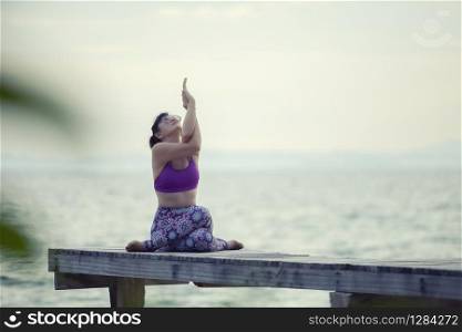 woman playing yoga on wooded pier against plain sea background