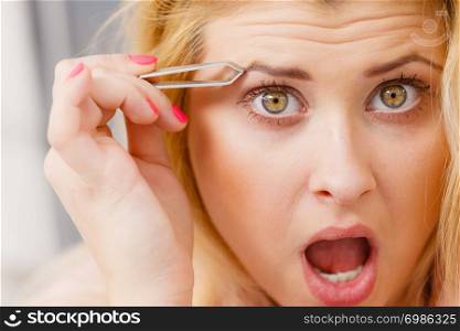 Woman plucking eyebrows depilating with tweezers closeup part of face. Girl tweezing removing her facial hairs... Woman tweezing eyebrows depilating with tweezers