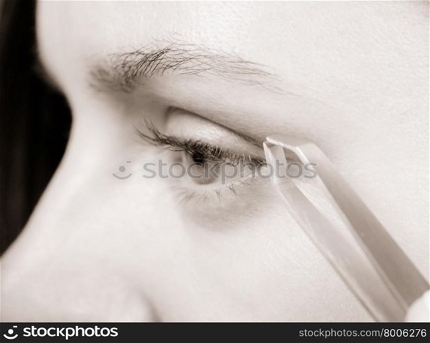 Woman plucking eyebrows depilating with tweezers closeup part of face. Girl tweezing eyebrows, black &amp;amp; white photo