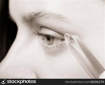 Woman plucking eyebrows depilating with tweezers closeup part of face. Girl tweezing eyebrows, black &amp;amp; white photo