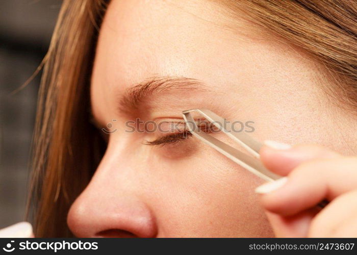 Woman plucking eyebrows depilating with tweezers closeup part of face. Girl tweezing eyebrows.. Woman tweezing eyebrows depilating with tweezers