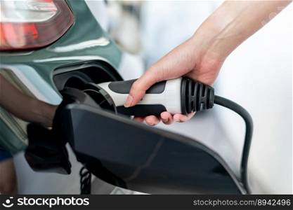 Woman plugged cable charging an electric car at home.
