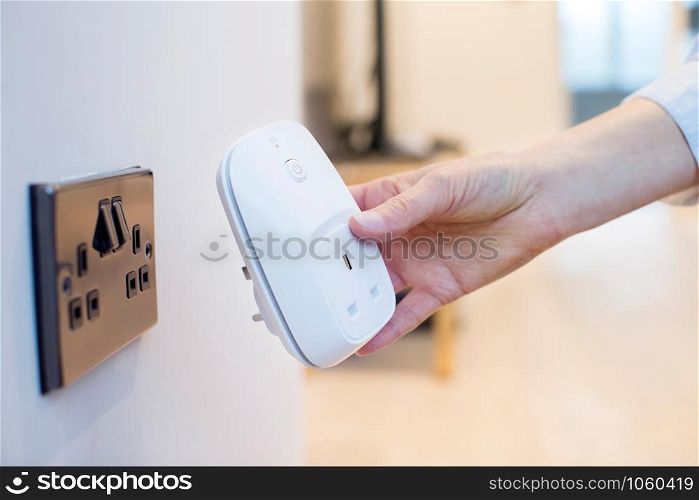 Woman Plugging Smart Plug Into Wall Socket At Home