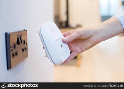 Woman Plugging Smart Plug Into Wall Socket At Home