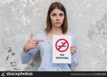 woman pointing finger no smoking poster standing near weathered wall