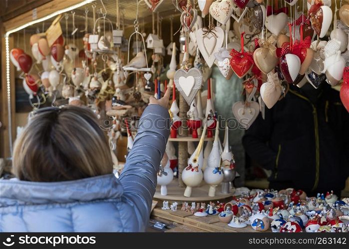 Woman pointing her finger on christmas decorations out of felt on the christmas market of meran in South Tyrol to show them her friends