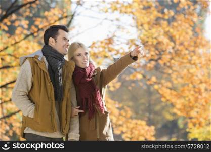Woman pointing while standing with man in park during autumn
