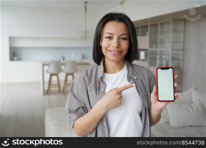 Woman points to phone screen with copy space. Conceptual portrait of young emotional girl. Mockup for smartphone advertising banner. Handsome european girl is using mobile app. Modern interior.. Woman points to phone screen with copy space. Mockup for smartphone advertising banner.