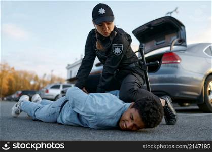 Woman police officer in uniform arresting suspicious young car driver wringing his hands back. Police officer arresting suspicious young car driver