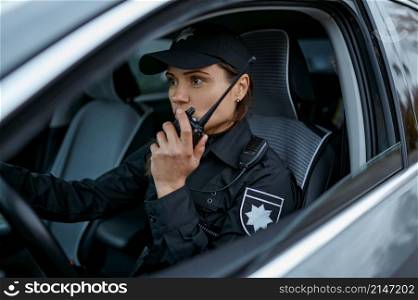 Woman police officer using walkie-talkie portable radio driving in car. Female cop patrolling street. Policewoman using radio patrolling street in car