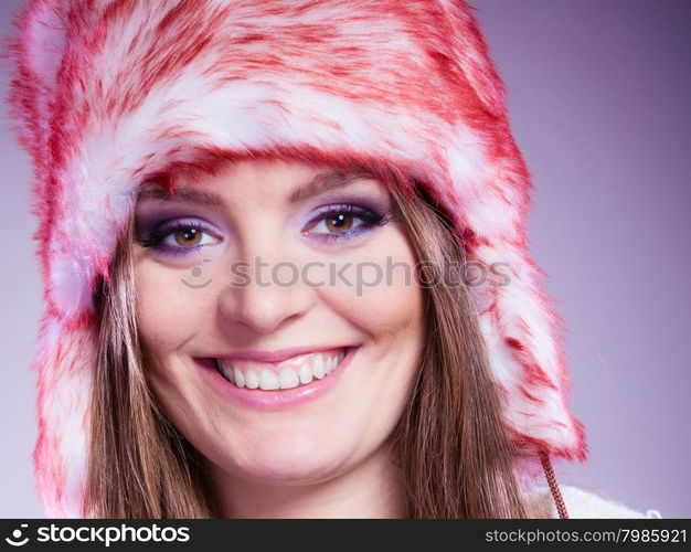 Woman portrait in winter cap. Close up portrait of attractive smiling young woman in fur winter cap with purple violet make up in studio. Wintertime.