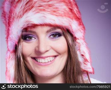 Woman portrait in winter cap. Close up portrait of attractive smiling young woman in fur winter cap with purple violet make up in studio. Wintertime.