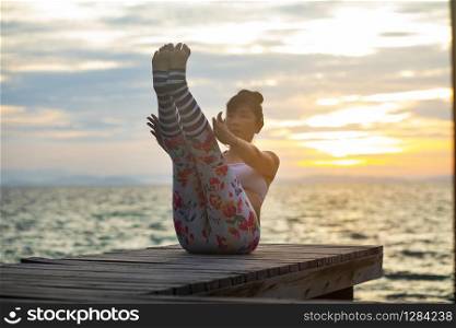woman pose yoga on wooden pier at sea side against beautiful sun rising sky