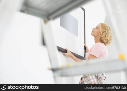 Woman positioning picture frame on wall