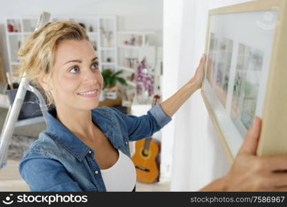 woman positioning picture frame on wall