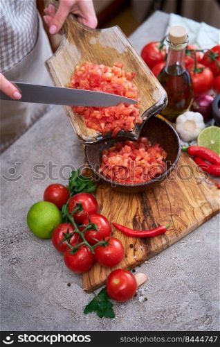 woman pouring chopped blanched tomatoes to wooden bowl.. woman pouring chopped blanched tomatoes to wooden bowl