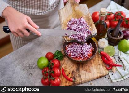 woman pouring chopped onion to wooden bowl with tomatoes.. woman pouring chopped onion to wooden bowl with tomatoes
