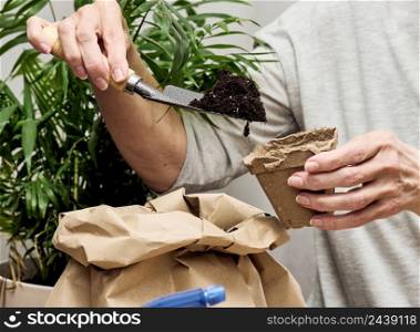 Woman pouring earth into a paper cup for planting seeds at home
