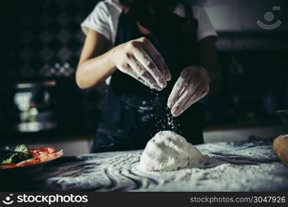 Woman pouring flour on dough while kneads preparing for make pizza. Cooking concept.