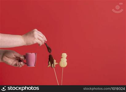 Woman pouring melted chocolate over Christmas tree-shaped cookie, on a red background. Glazing gingerbread cookies. Xmas traditional sweets.