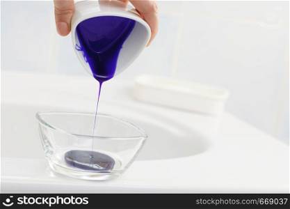 Woman pouring purple hair dye or shampoo toner into white bowl. Hygiene object concept.. Woman pouring purple hair dye or shampoo