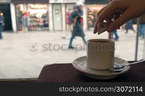 Woman pouring sugar into coffee and stirring it up. Enjoying hot drink in cafe with view to the street